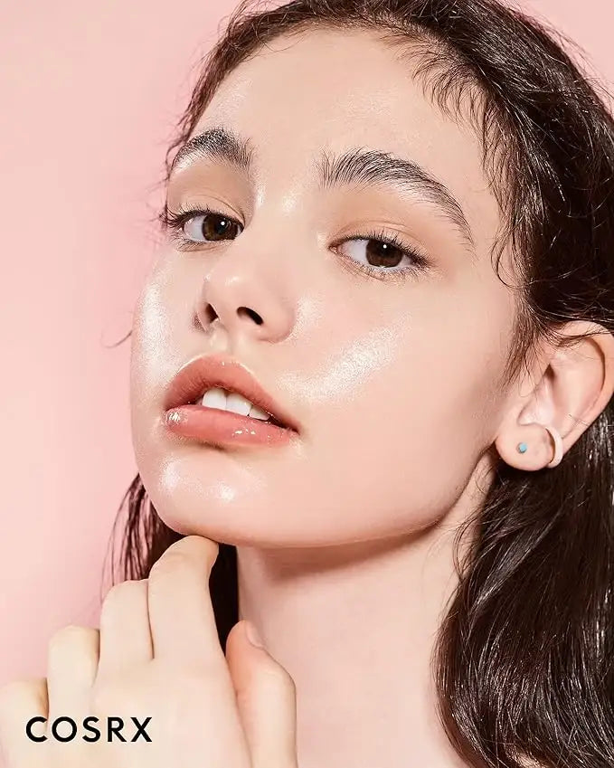 Close-up of woman with glowing dewy skin, minimal makeup, and glossy lips against pink background