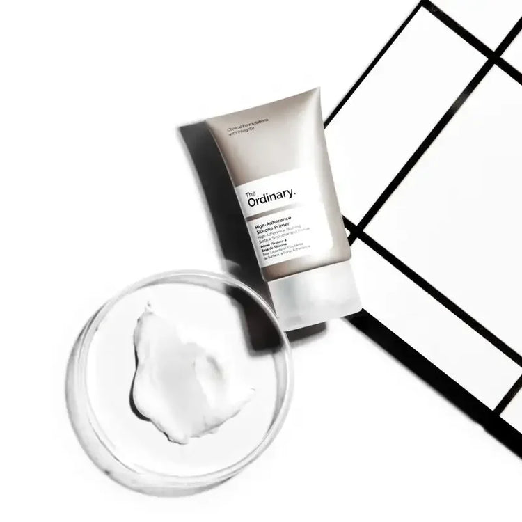 The Ordinary High-Adherence Silicone Primer tube next to a clear dish with creamy skincare product