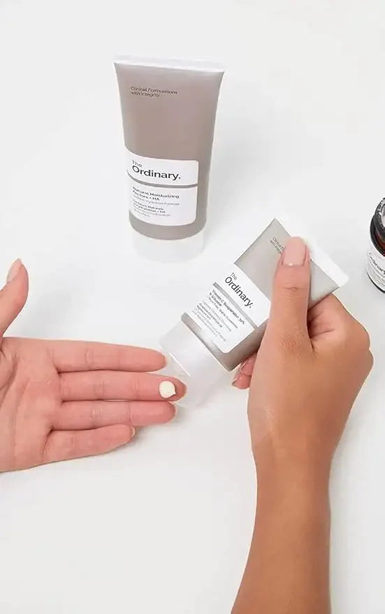 Hand applying The Ordinary Natural Moisturizing Factors cream, white background, skincare product