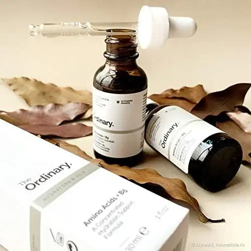 The Ordinary Amino Acids serum bottles with dropper on a surface with dry leaves, skincare product