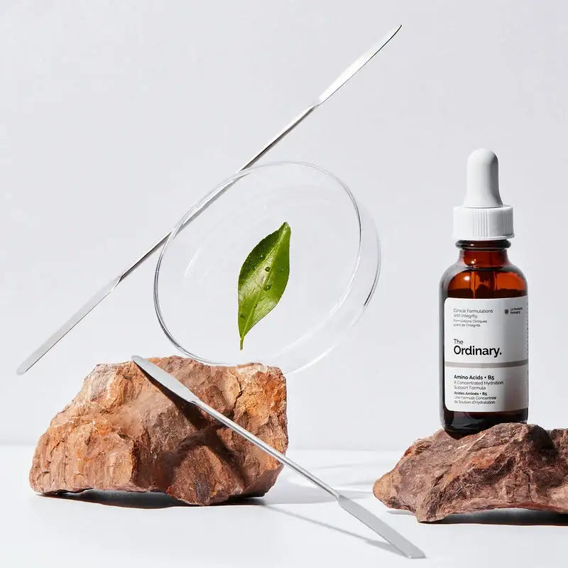 The Ordinary serum dropper bottle with natural rocks, glass plate, and green leaf for skincare.