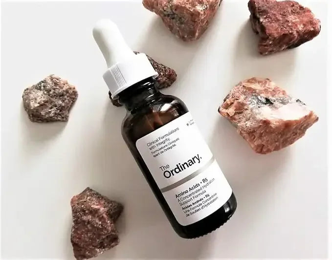 The Ordinary amino acids serum bottle with dropper, surrounded by natural stone pieces