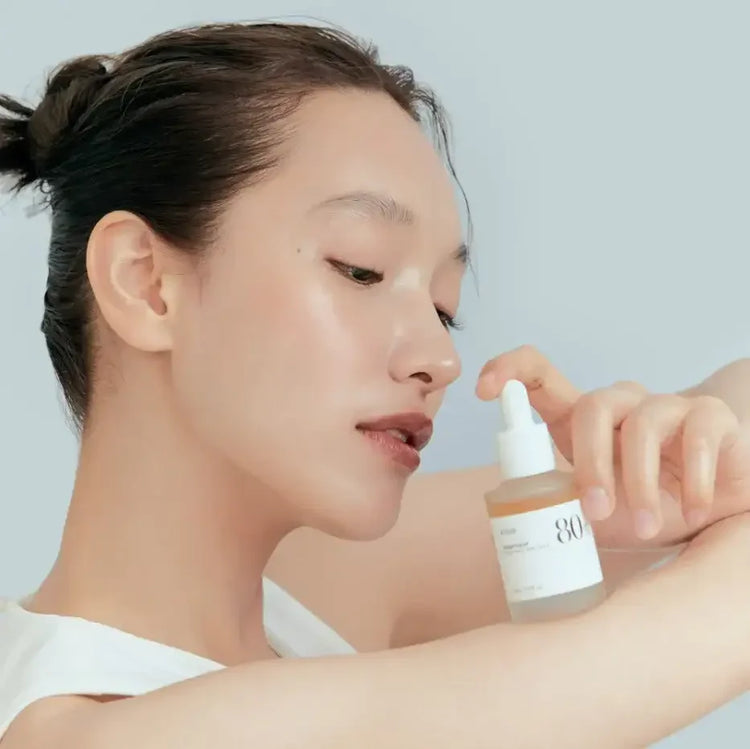 Woman applying Korean skincare serum with dropper to arm, clear glowing skin