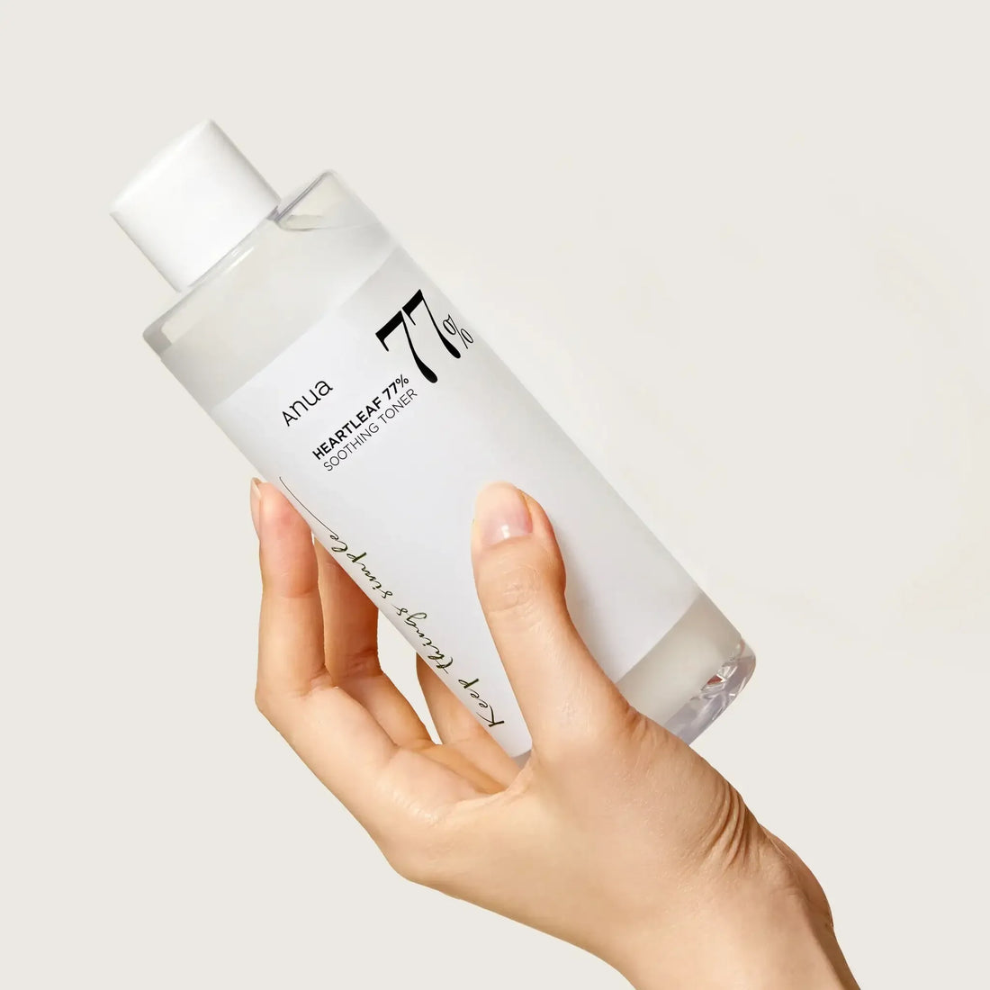 Hand holding Anua Heartleaf 77% Soothing Toner bottle against a plain background