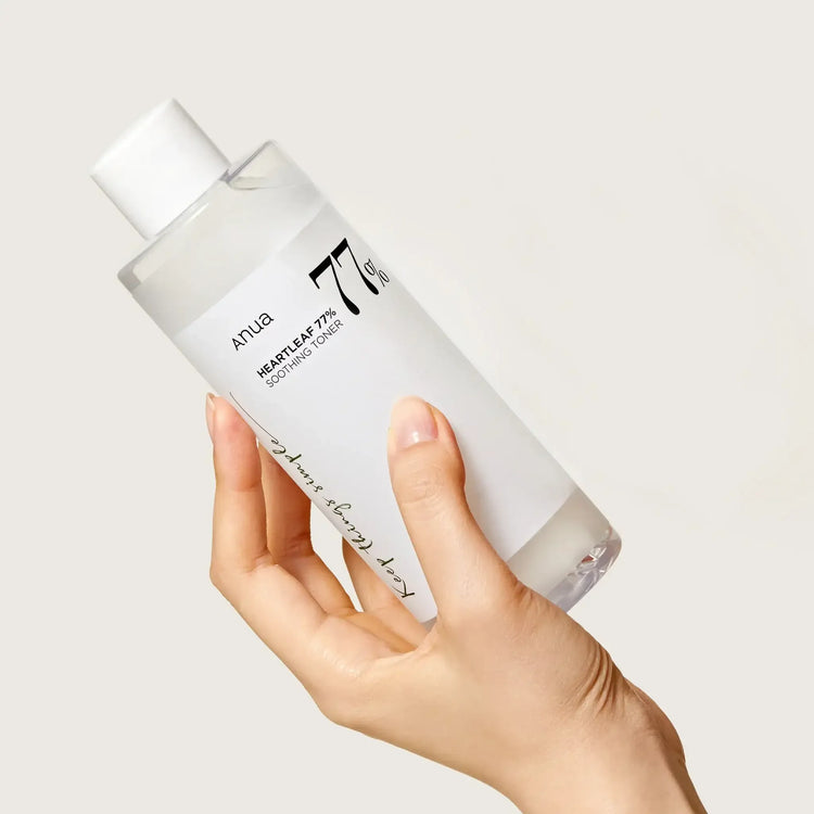 Hand holding Anua Heartleaf 77% Soothing Toner bottle against a plain background