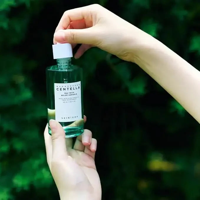 Hand holding SKIN1004 Centella ampoule skincare bottle with green nature background