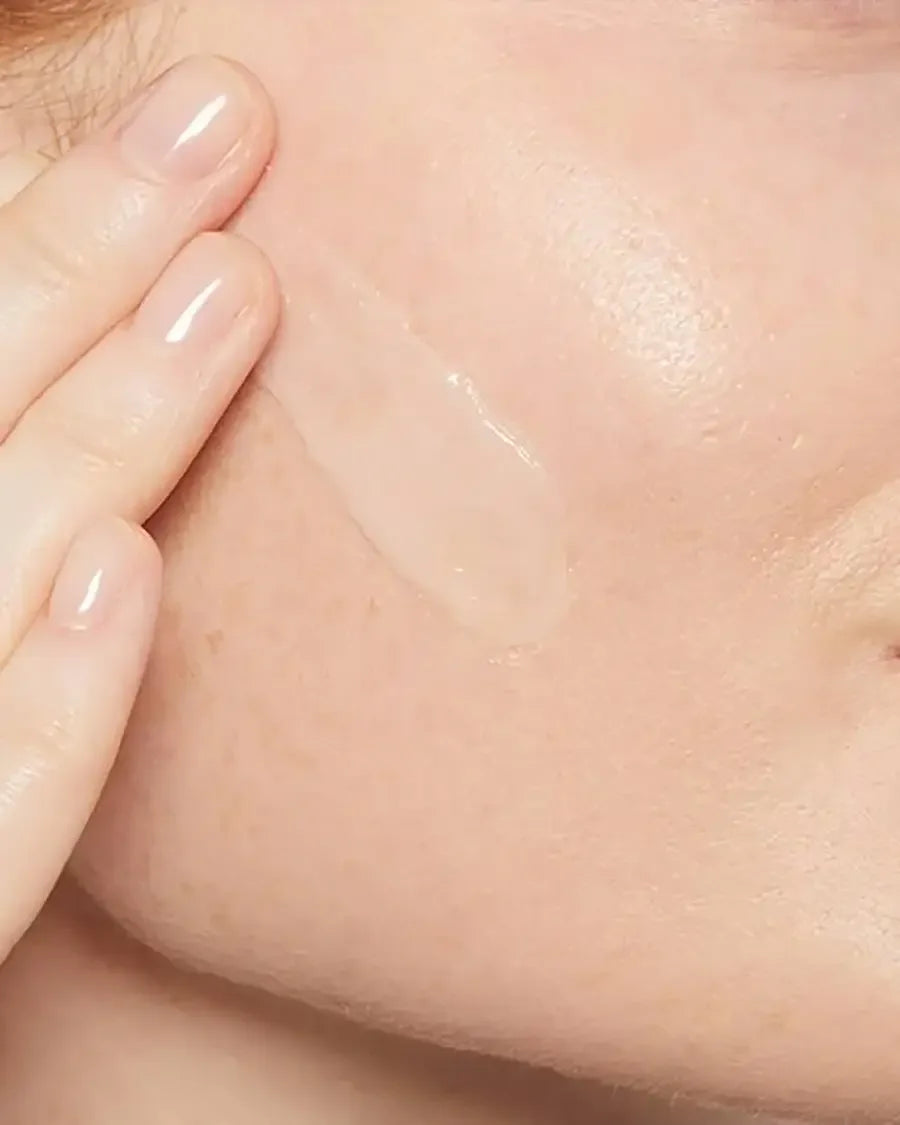 Close-up of a hand applying clear skincare serum to cheek, smooth healthy skin visible