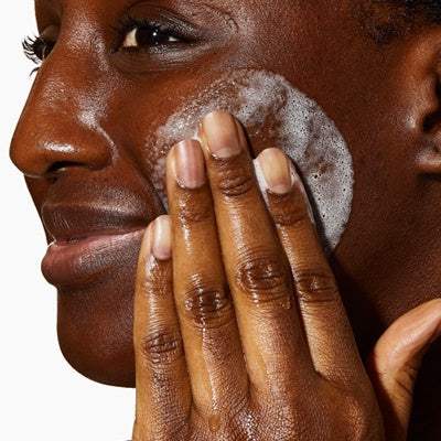 Woman cleansing face with foaming facial cleanser, skincare routine close-up