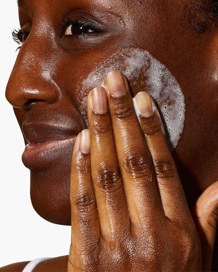 Woman applying foaming facial cleanser to her cheek, skincare routine close-up